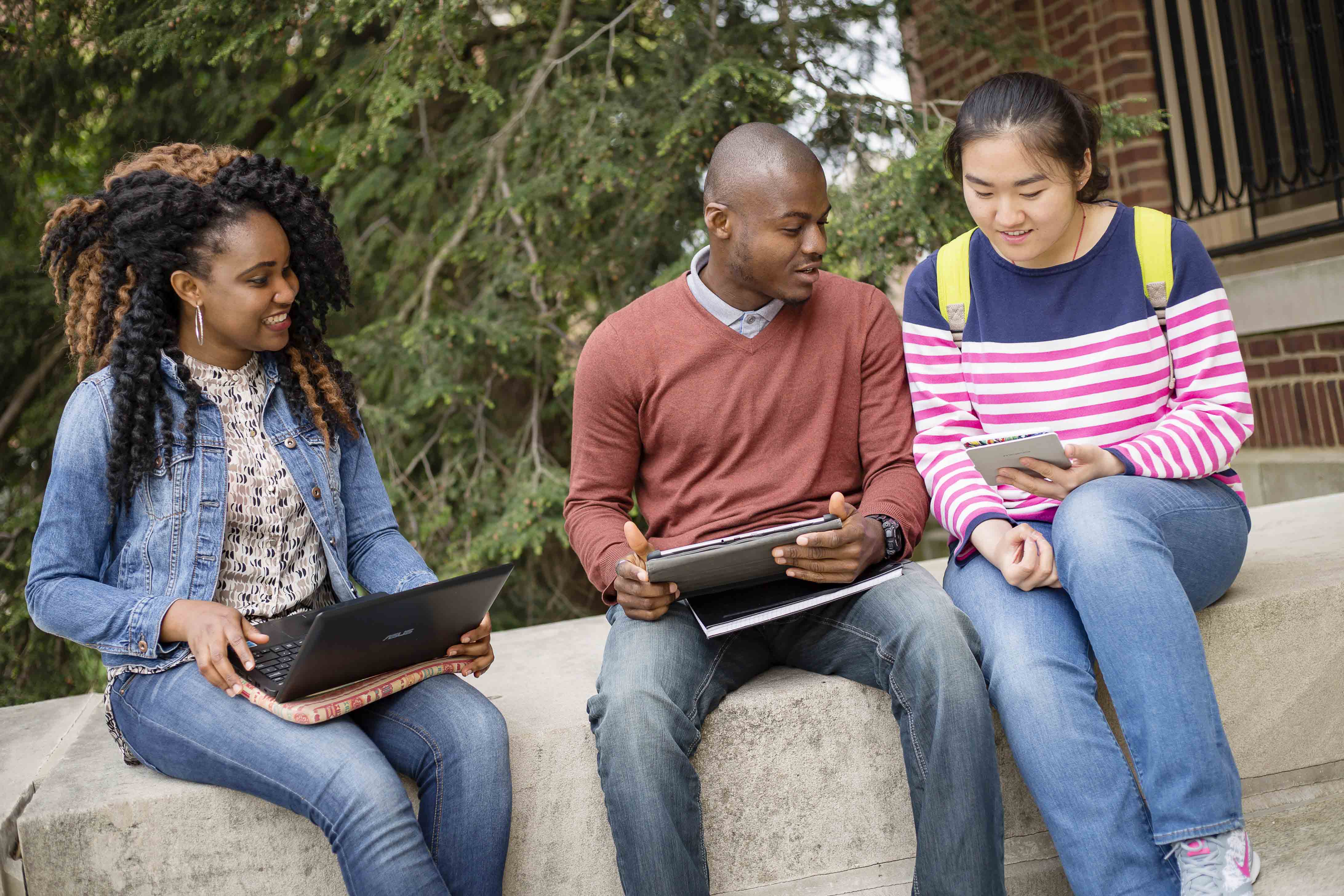 three people sitting outside with laptops