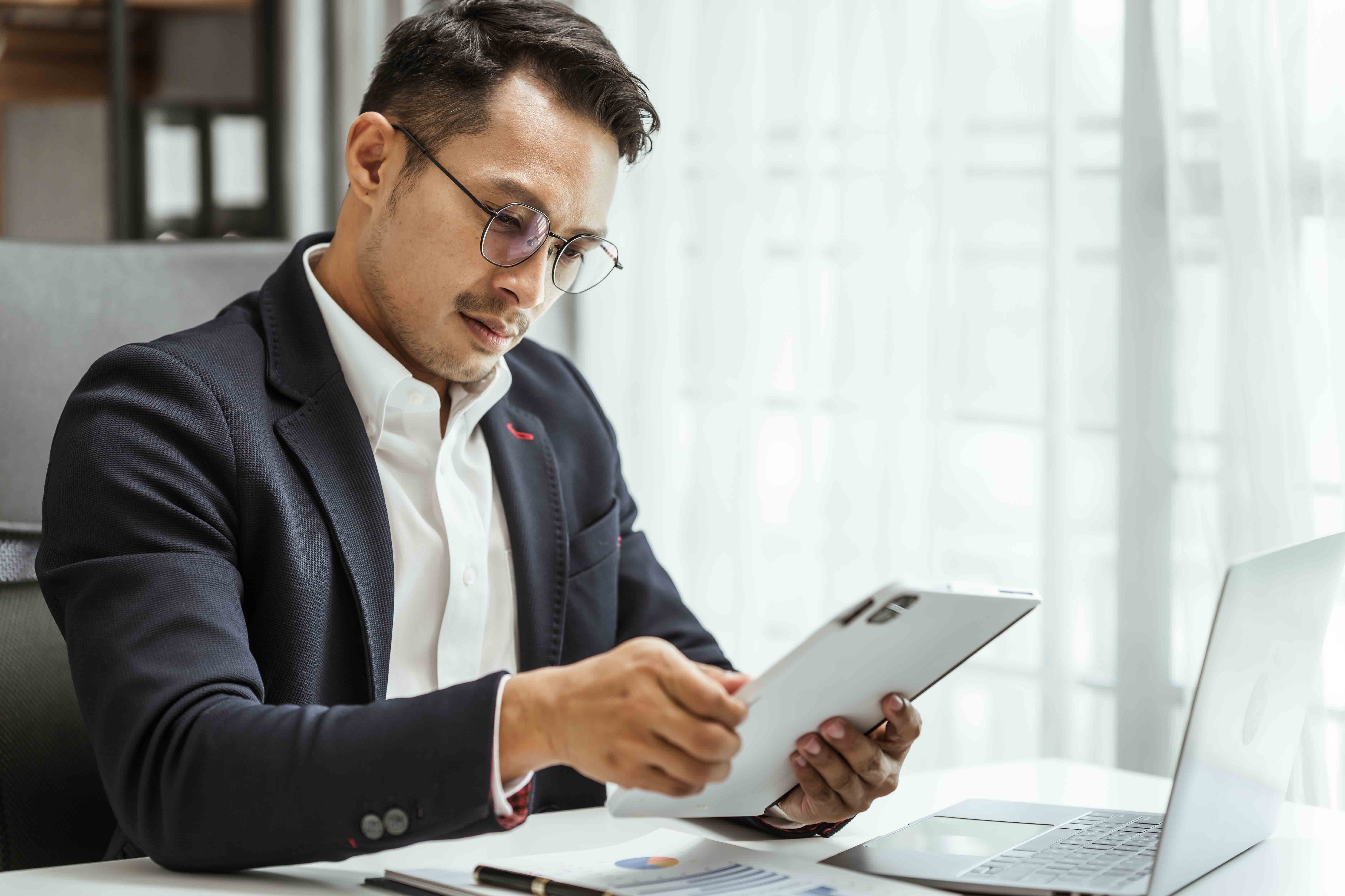 person in suit looking at tablet with laptop nearby