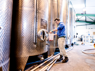Man wearing a blue shirt standing near a fermentation tank